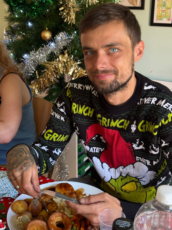 Man wearing a Grinch sweater at a festive table with food and Christmas decorations.