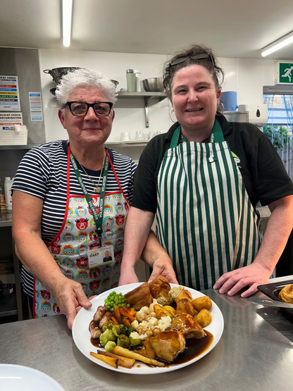 Two people in a kitchen holding a plate of food