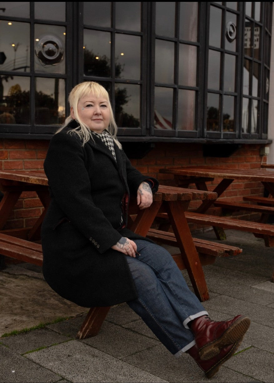 Woman sitting on a wooden bench in front of a building with large windows.